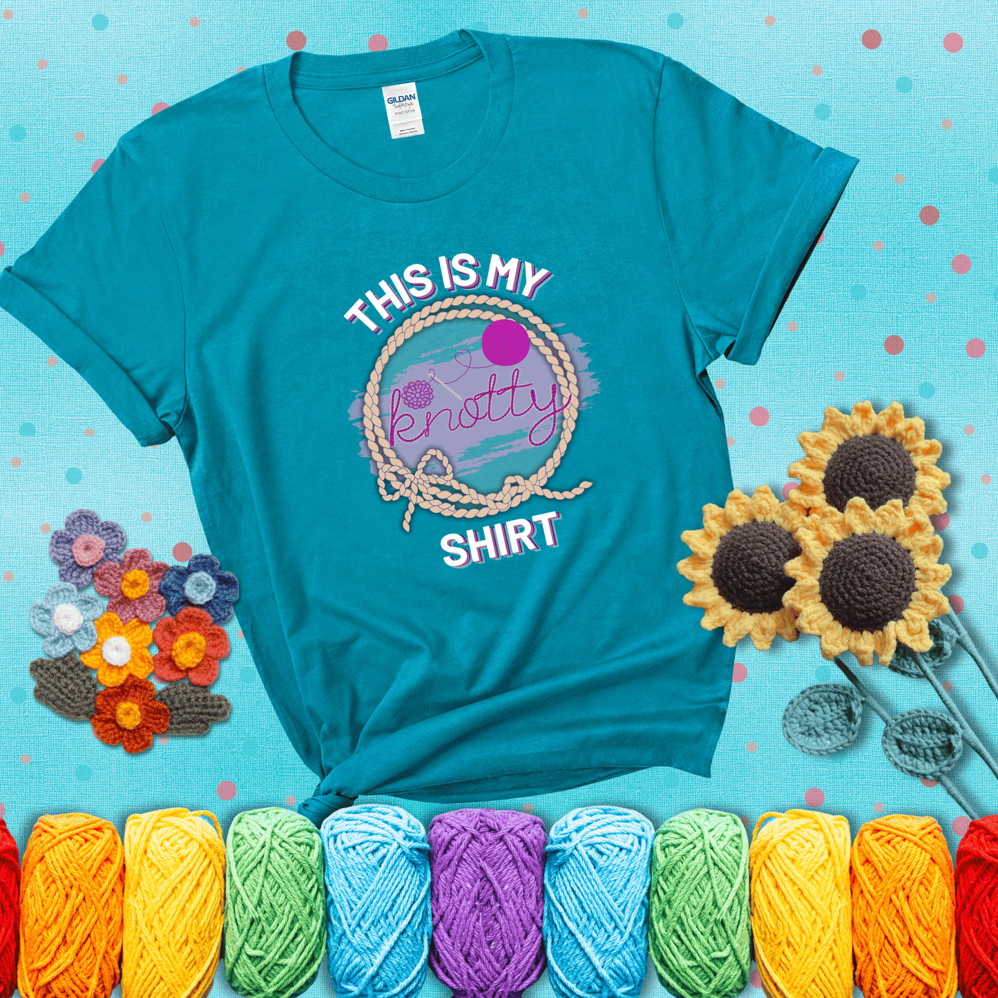 A playful design with the phrase "This is my knotty shirt" inside a rope circle, featuring a yarn ball and a crochet hook forming the word "knotty" showing a blue-green tee with a teal sunflower background