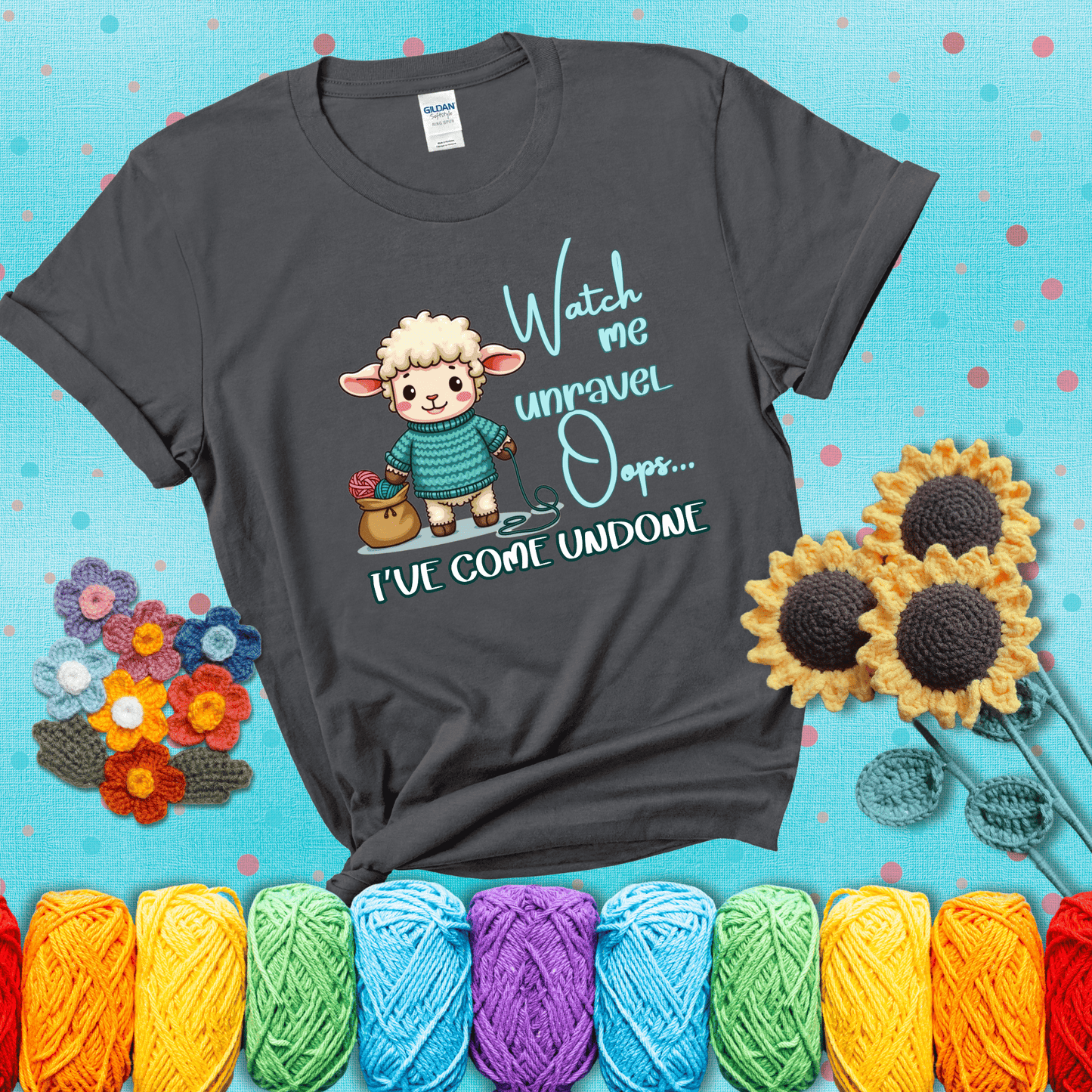 Cute sheep holding yarn looks startled with the phrase “Watch me unravel… Oops, I’ve come undone.” Perfect mix of whimsy and yarn life chaos, showing a dark grey tee with a teal sunflower background
