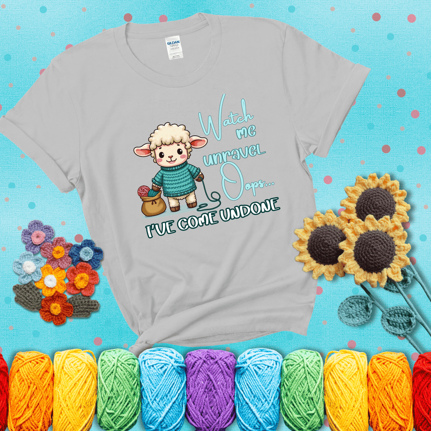 Cute sheep holding yarn looks startled with the phrase “Watch me unravel… Oops, I’ve come undone.” Perfect mix of whimsy and yarn life chaos, showing a light grey tee with a teal sunflower background