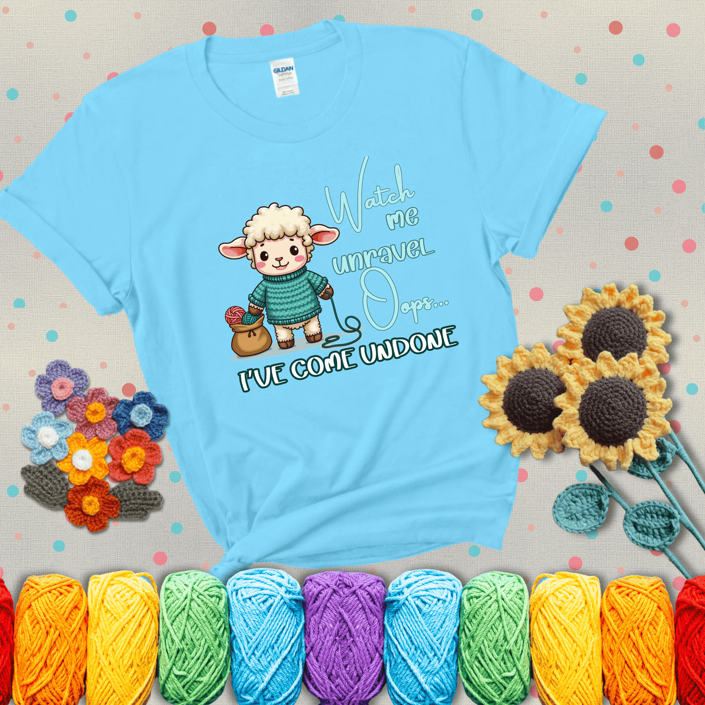 Cute sheep holding yarn looks startled with the phrase “Watch me unravel… Oops, I’ve come undone.” Perfect mix of whimsy and yarn life chaos, showing a light blue tee with grey sunflower background