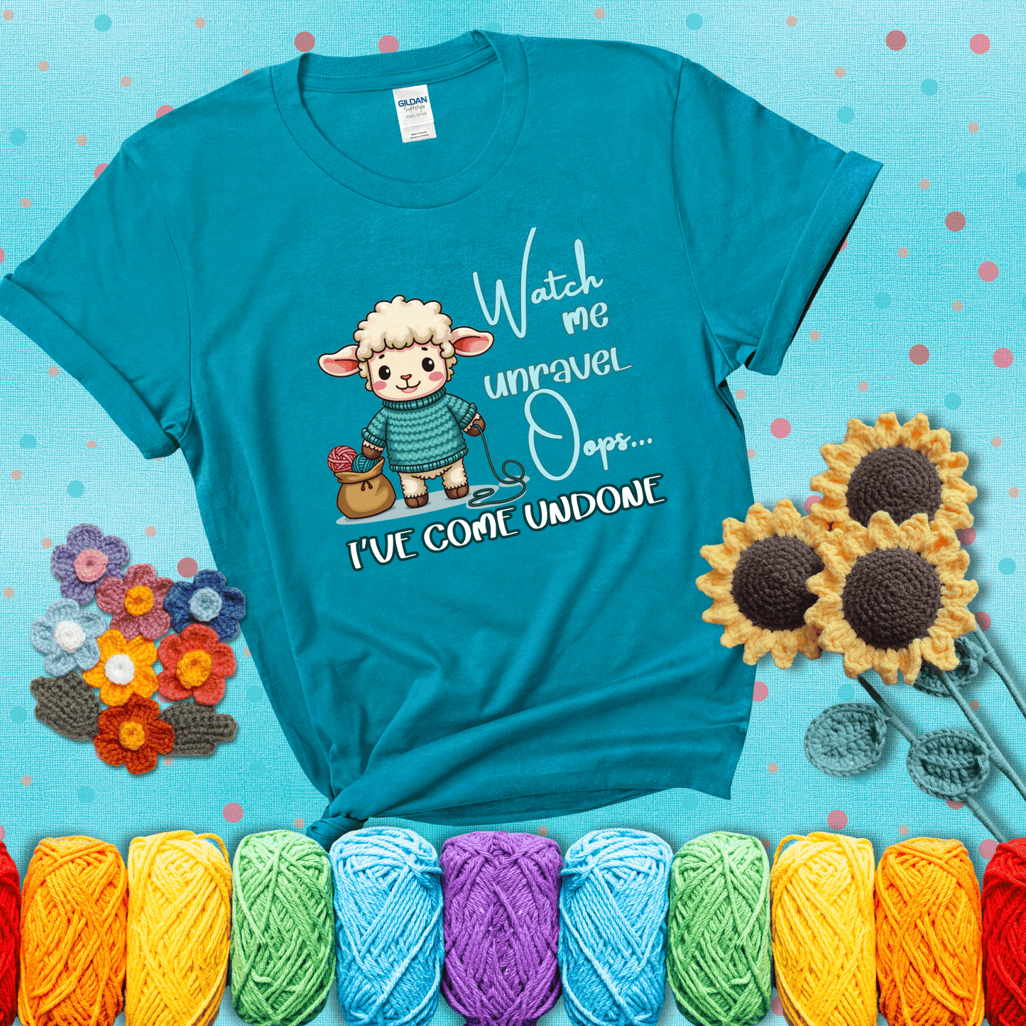 Cute sheep holding yarn looks startled with the phrase “Watch me unravel… Oops, I’ve come undone.” Perfect mix of whimsy and yarn life chaos, showing a blue-green tee with a teal sunflower background