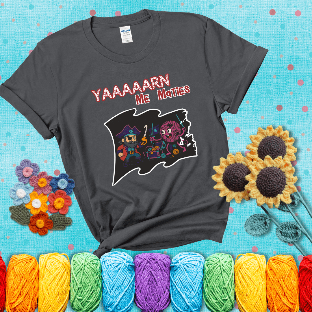 A pirate with a crochet hook for a hand duels a fierce yarn ball wielding knitting needles, standing in front of a treasure chest filled with yarn showing a dark grey tee with a teal sunflower background