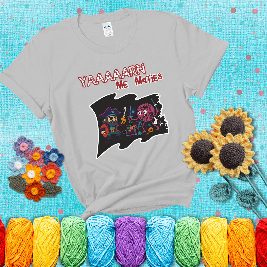 A pirate with a crochet hook for a hand duels a fierce yarn ball wielding knitting needles, standing in front of a treasure chest filled with yarn showing a light grey tee with a teal sunflower background