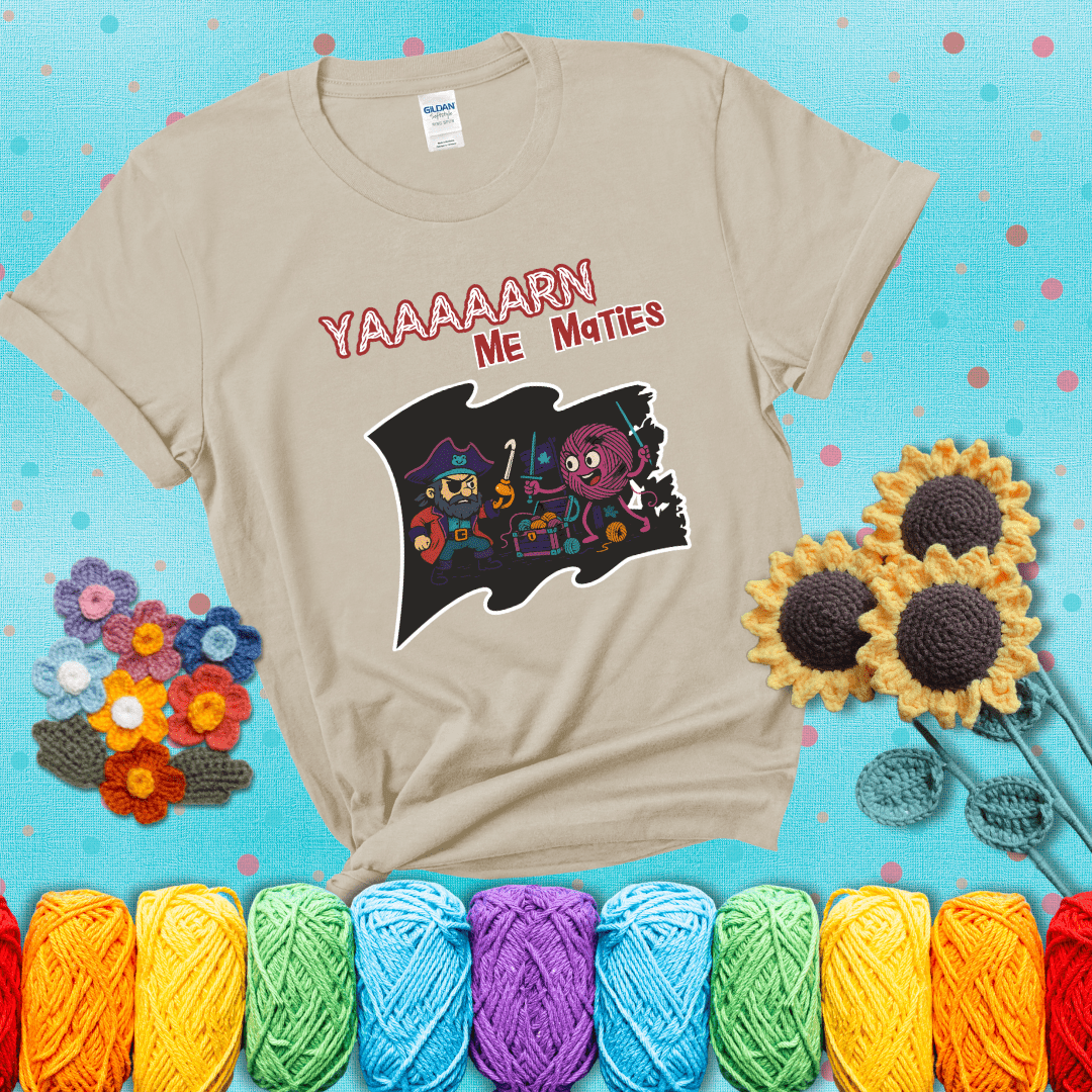 A pirate with a crochet hook for a hand duels a fierce yarn ball wielding knitting needles, standing in front of a treasure chest filled with yarn showing a beige tee with a teal sunflower background