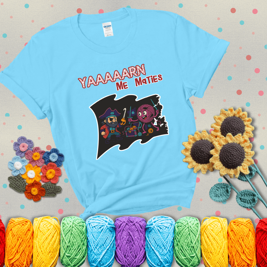 A pirate with a crochet hook for a hand duels a fierce yarn ball wielding knitting needles, standing in front of a treasure chest filled with yarn showing a light blue tee with grey sunflower background