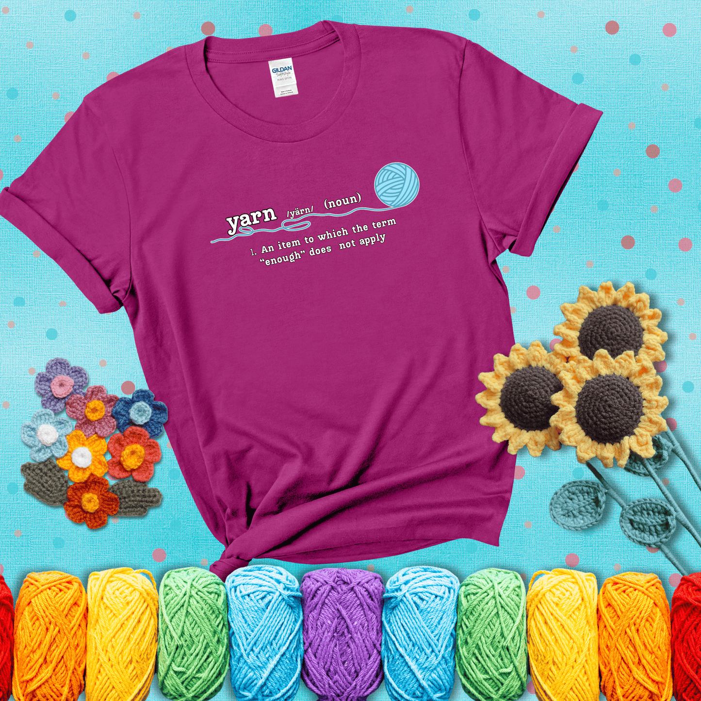 A definition-style graphic showing the word "yarn" as a noun, with the definition “An item to which the term ‘enough’ does not apply,” and a ball of blue yarn with a loose strand showing a magenta tee with a teal sunflower background