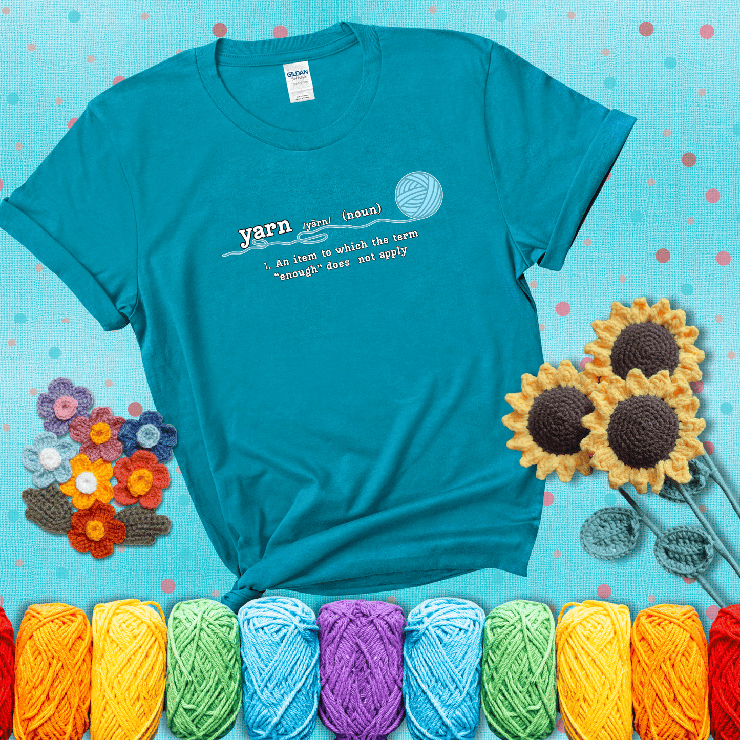 A definition-style graphic showing the word "yarn" as a noun, with the definition “An item to which the term ‘enough’ does not apply,” and a ball of blue yarn with a loose strand showing a blue-green tee with a teal sunflower background