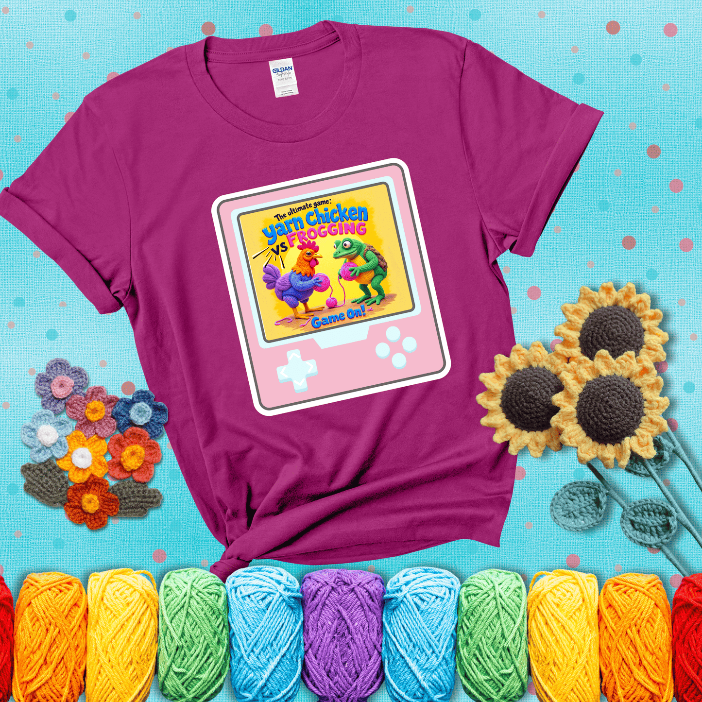 A colorful chicken and frog holding pink yarn face off inside a retro handheld game screen with the title “The ultimate game: Yarn Chicken vs. Frogging – Game On!” showing a magenta tee with a teal sunflower background