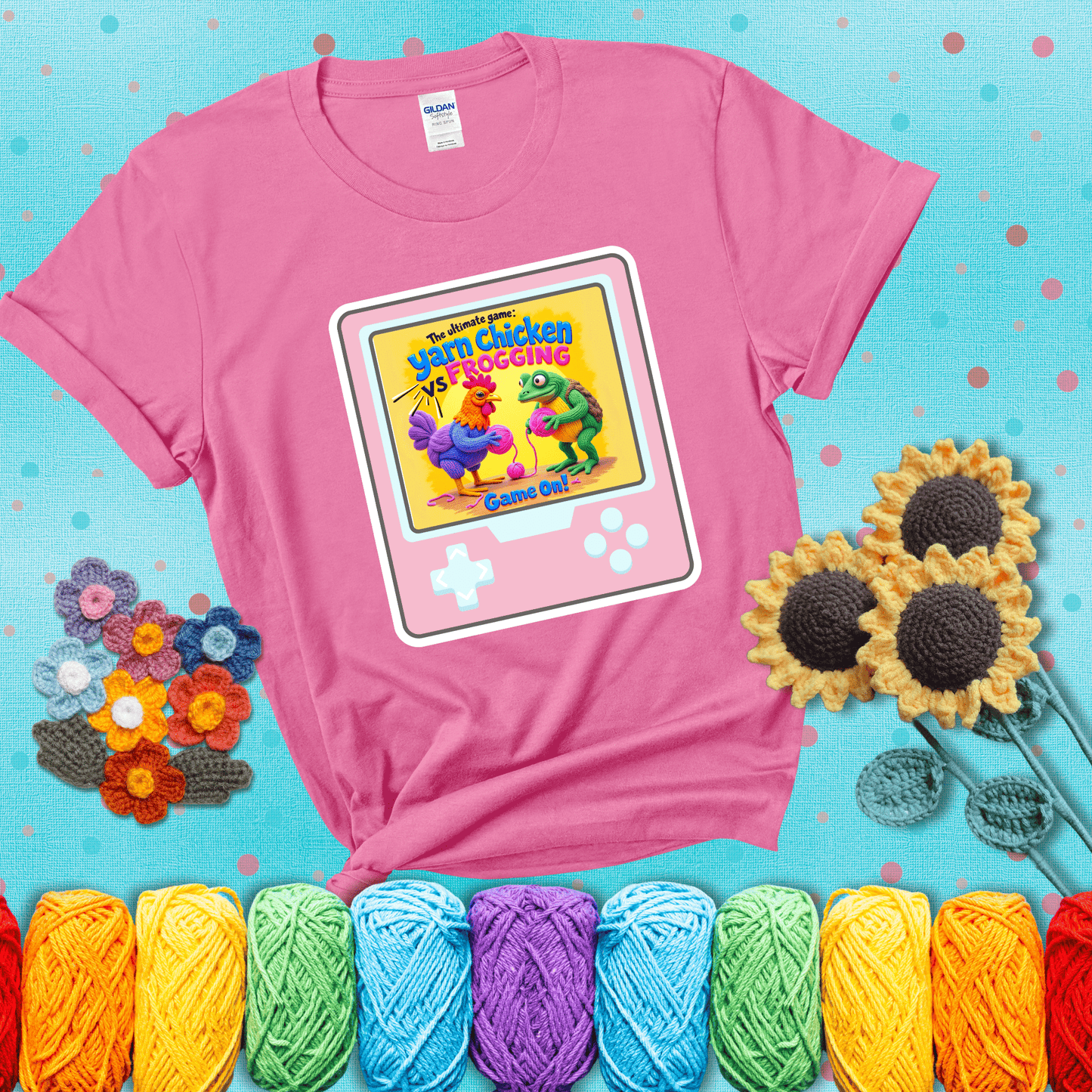 A colorful chicken and frog holding pink yarn face off inside a retro handheld game screen with the title “The ultimate game: Yarn Chicken vs. Frogging – Game On!” showing a pink tee with a teal sunflower background