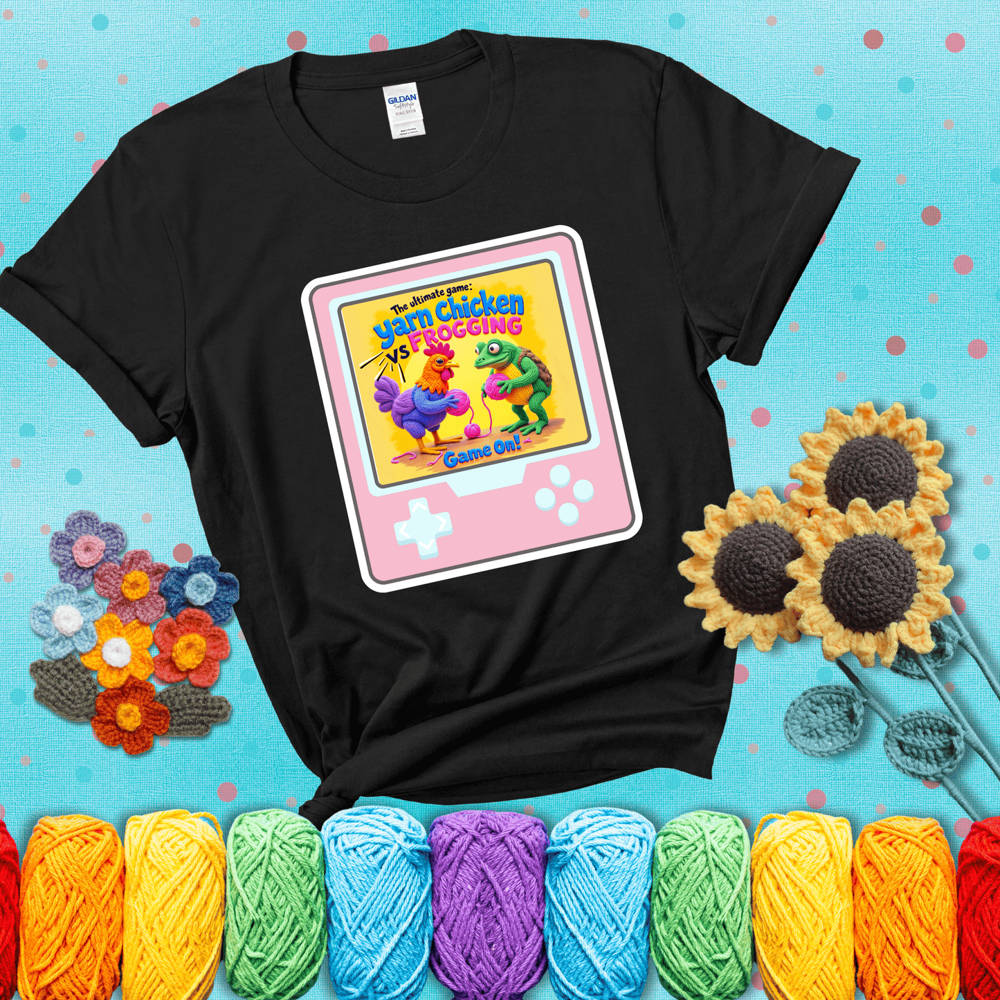 A colorful chicken and frog holding pink yarn face off inside a retro handheld game screen with the title “The ultimate game: Yarn Chicken vs. Frogging – Game On!” showing a black tee with a teal sunflower background