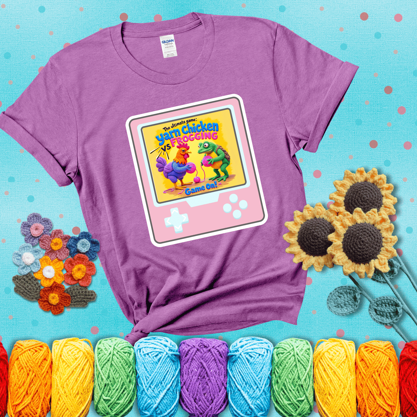 A colorful chicken and frog holding pink yarn face off inside a retro handheld game screen with the title “The ultimate game: Yarn Chicken vs. Frogging – Game On!” showing a light purple tee with a teal sunflower background