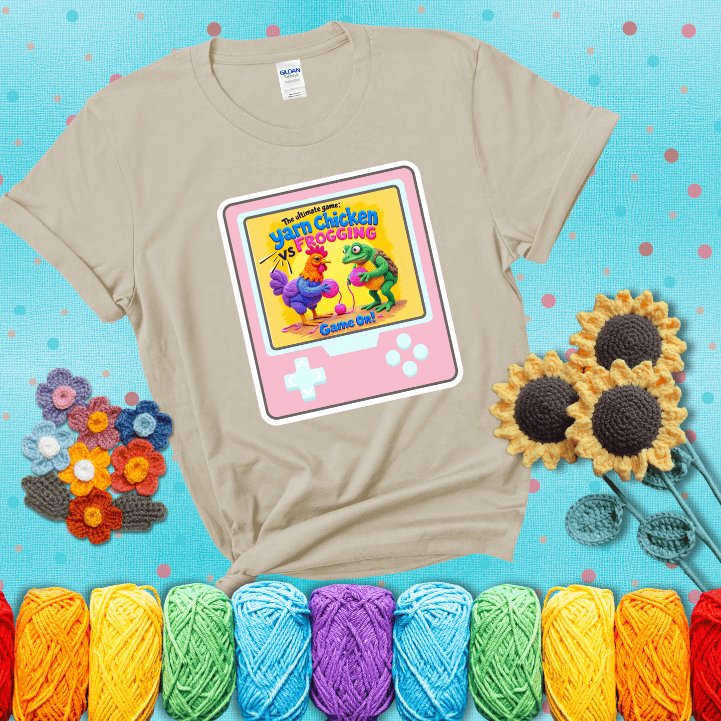 A colorful chicken and frog holding pink yarn face off inside a retro handheld game screen with the title “The ultimate game: Yarn Chicken vs. Frogging – Game On!” showing a beige tee with a teal sunflower background