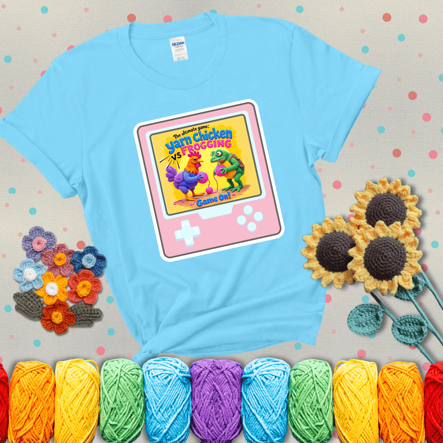 A colorful chicken and frog holding pink yarn face off inside a retro handheld game screen with the title “The ultimate game: Yarn Chicken vs. Frogging – Game On!” showing a light blue tee with grey sunflower background