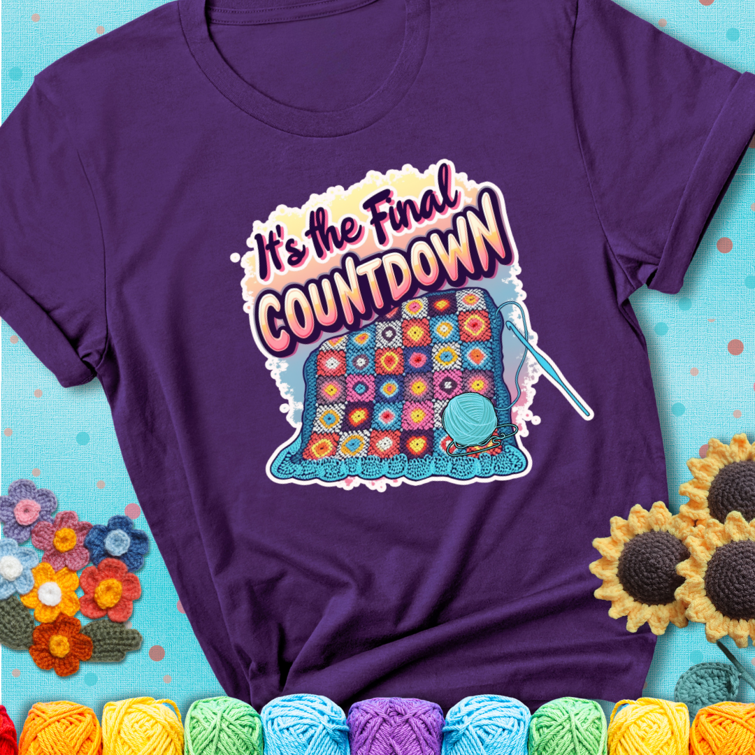 Purple t-shirt with a colorful crochet blanket in progress, blue yarn ball, crochet hook, and the phrase “It’s The Final Countdown.”