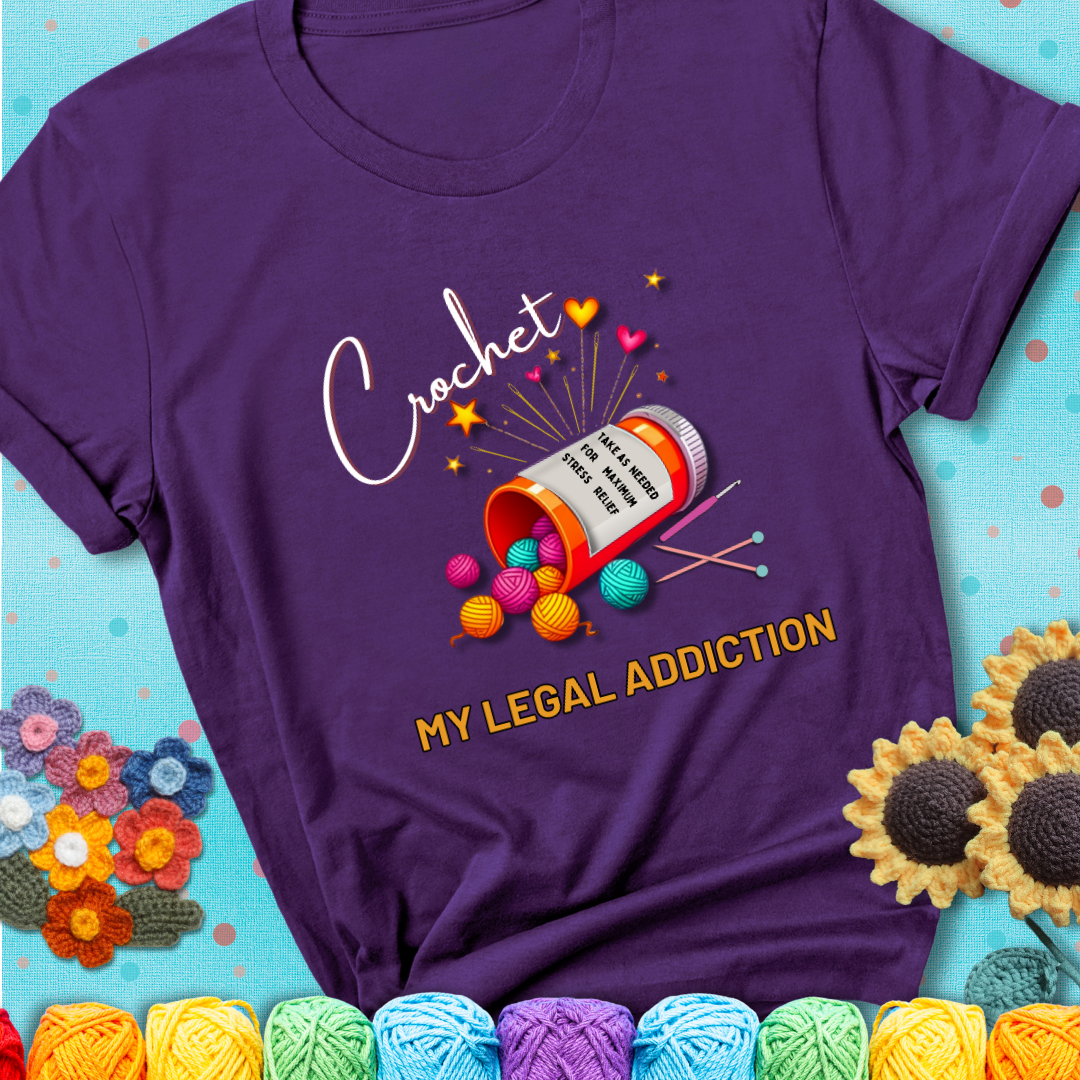 Purple t-shirt with a prescription bottle spilling colorful yarn balls, small crochet details, and the phrase “Crochet: My Legal Addiction.”