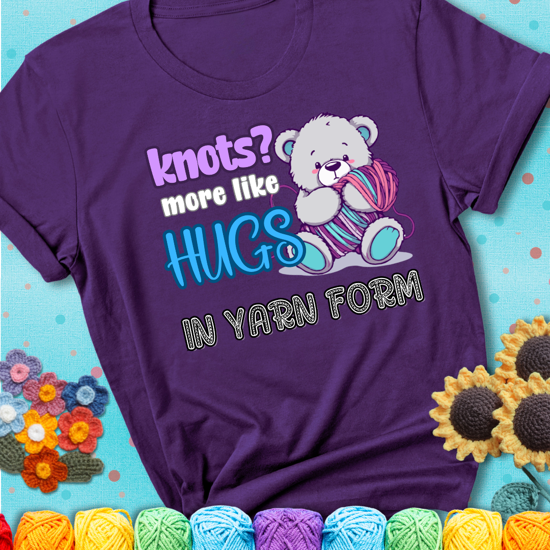 Cute teddy bear holding colorful yarn ball with hearts. Text reads: “Knots? More Like Hugs in Yarn Form.” Perfect for cozy gift-givers and yarn lovers, showing a purple tee with a teal sunflower background