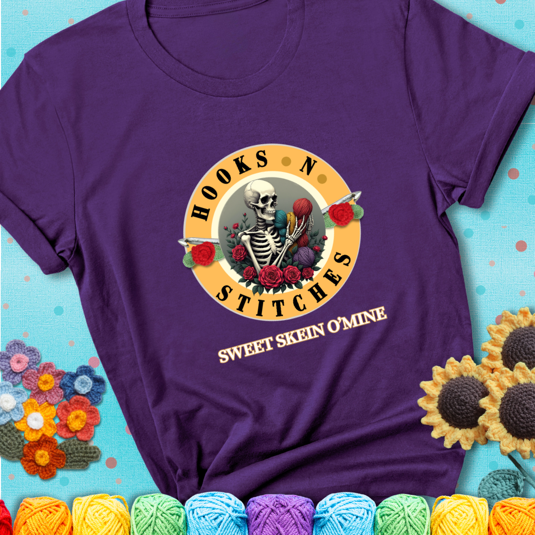 Purple t-shirt with a skeleton holding colorful yarn, roses, crochet hooks, and the phrases “Hooks ’N Stitches” and “Sweet Skein O’Mine.”