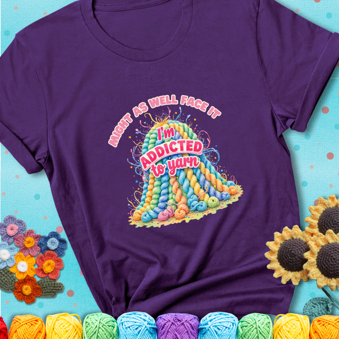 Purple t-shirt with a colorful mountain of pastel yarn hanks and the phrase “Might As Well Face It, I’m Addicted To Yarn” in pink and red lettering.