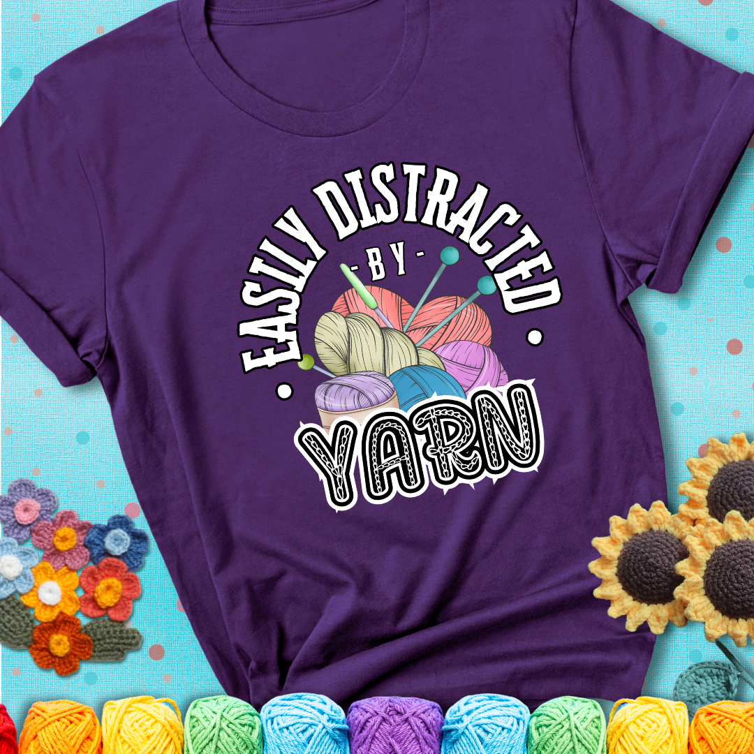 If yarn steals your focus every Design reads 'Easily Distracted By Yarn', perfect crochet gift for yarn lovers; showing a purple tee with a teal sunflower background