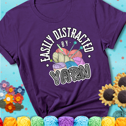 If yarn steals your focus every Design reads 'Easily Distracted By Yarn', perfect crochet gift for yarn lovers; showing a purple tee with a teal sunflower background