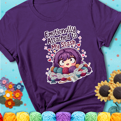 Adorable character with wide eyes hugging a yarn stash wrapped in chains and a heart-shaped lock, with the text “Emotionally Attached to My Stash”  on a purple tee.