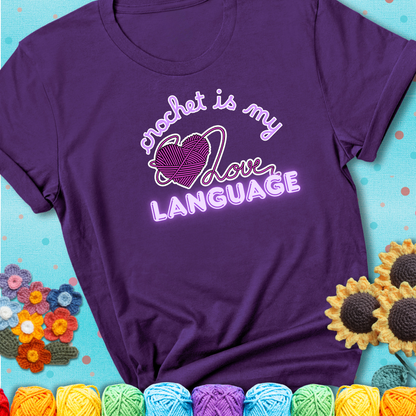 Say it with stitches Design reads 'Crochet Is My Love Language', perfect crochet gift for yarn lovers; showing a purple tee with a teal sunflower background