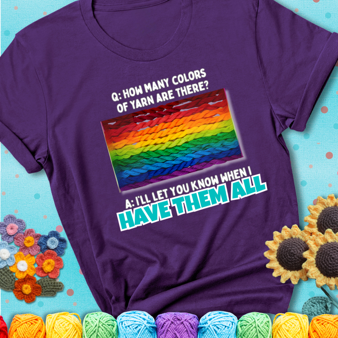 Purple t-shirt with rainbow skeins of yarn stacked in color gradient with playful question: “How many colors of yarn are there?” Answer: “I'll let you know when I have them all.”