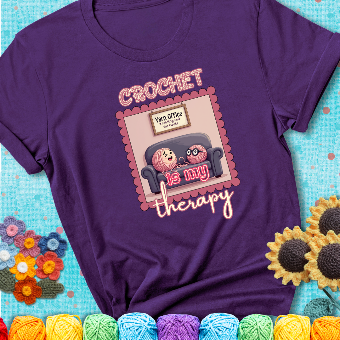 Purple t-shirt showing a simple text design with yarn cartoon figures. Text reads: “Crochet is My Therapy.” A calming tee for fiber lovers who find healing in every stitch.