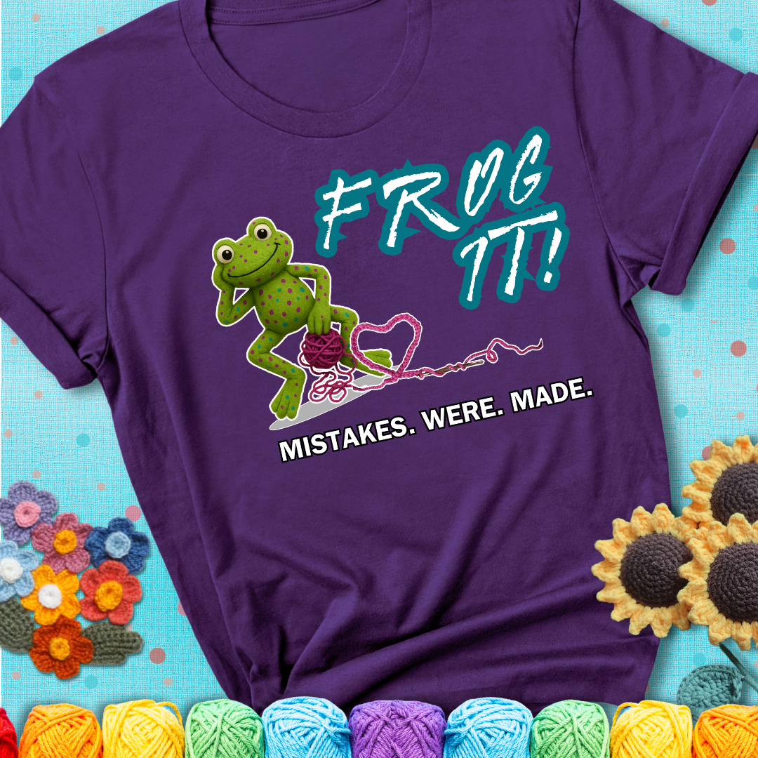 Green frog with yarn and heart-shaped loop. Text reads: “Frog It! Mistakes Were Made.” A playful crochet tee for anyone who's ever had to rip it back, showing a purple tee with a teal sunflower background