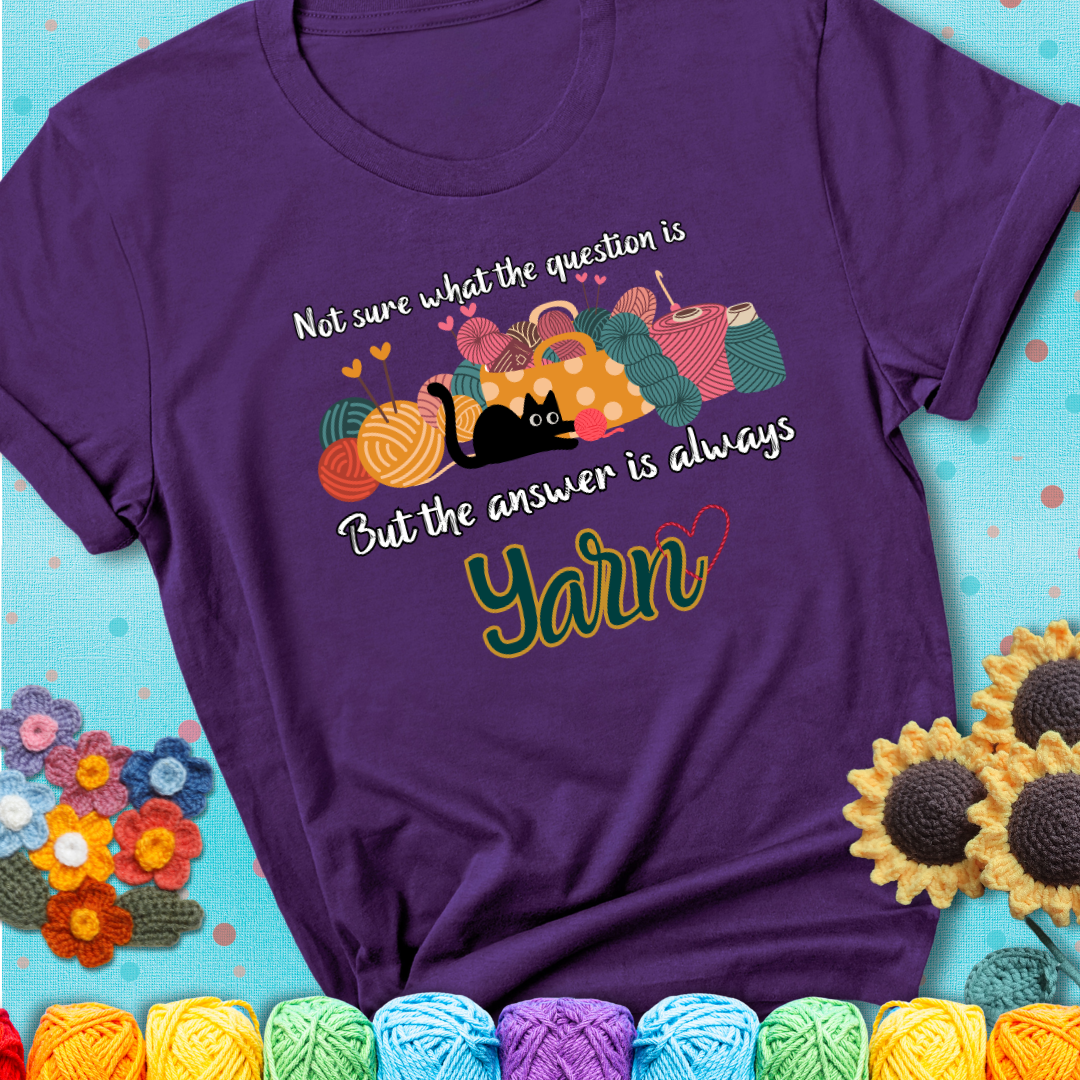 Purple t-shirt with a black cat beside a basket of colorful yarn and the phrase, “Not Sure What The Question Was, But The Answer Is Yarn.”