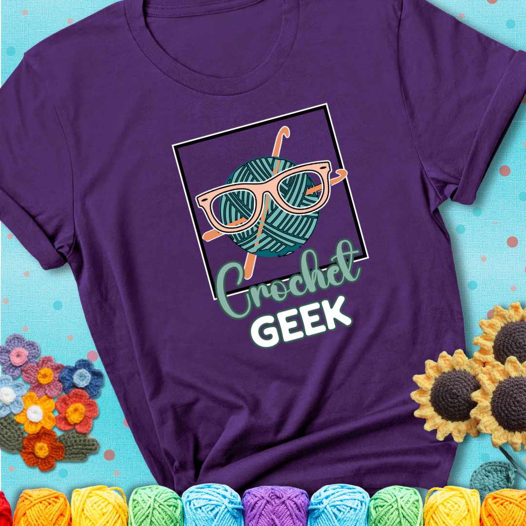 A teal yarn ball with crisscrossed hooks wears oversized nerdy glasses with the phrase “Crochet Geek” in bold, fun text below on a purple t-shirt.