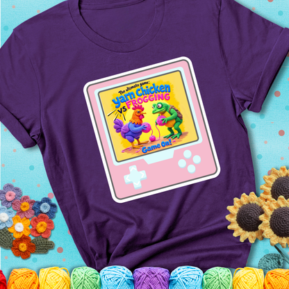 A purple t-shirt featuring a cartoon yarn chicken and frog face off with text “Yarn Chicken vs Frogging: Game On!” on a retro, handheld video game meets crochet humor battle design.
