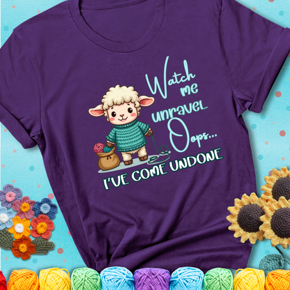 Purple t-shirt with a cute sheep holding yarn looks startled with the phrase “Watch me unravel… Oops, I’ve come undone.” Perfect mix of whimsy and yarn life chaos.