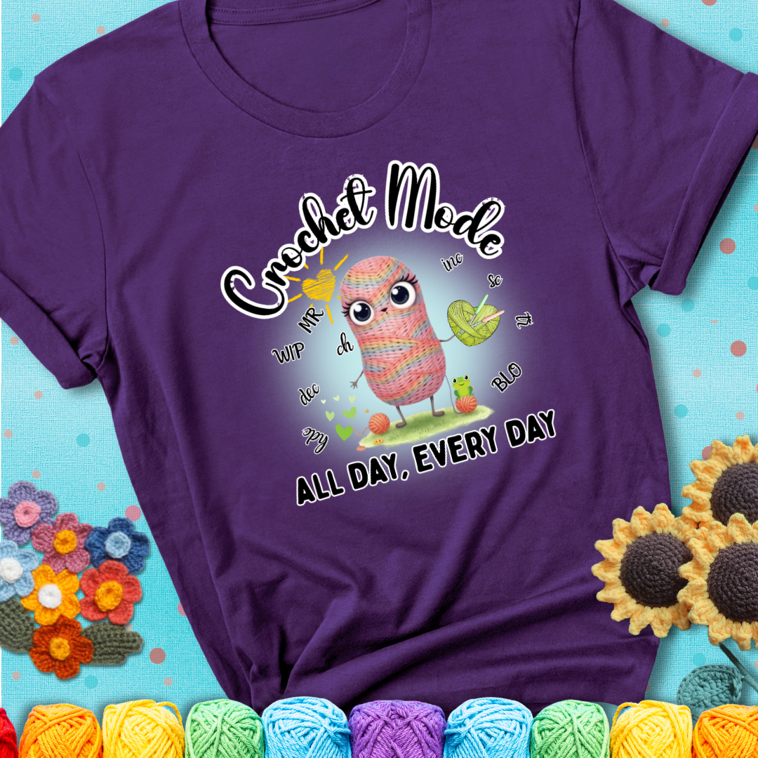 Purple t-shirt with a kawaii-style rainbow yarn character surrounded by crochet stitch abbreviations and holding a yarn heart, with text “Crochet Mode All Day, Every Day.”
