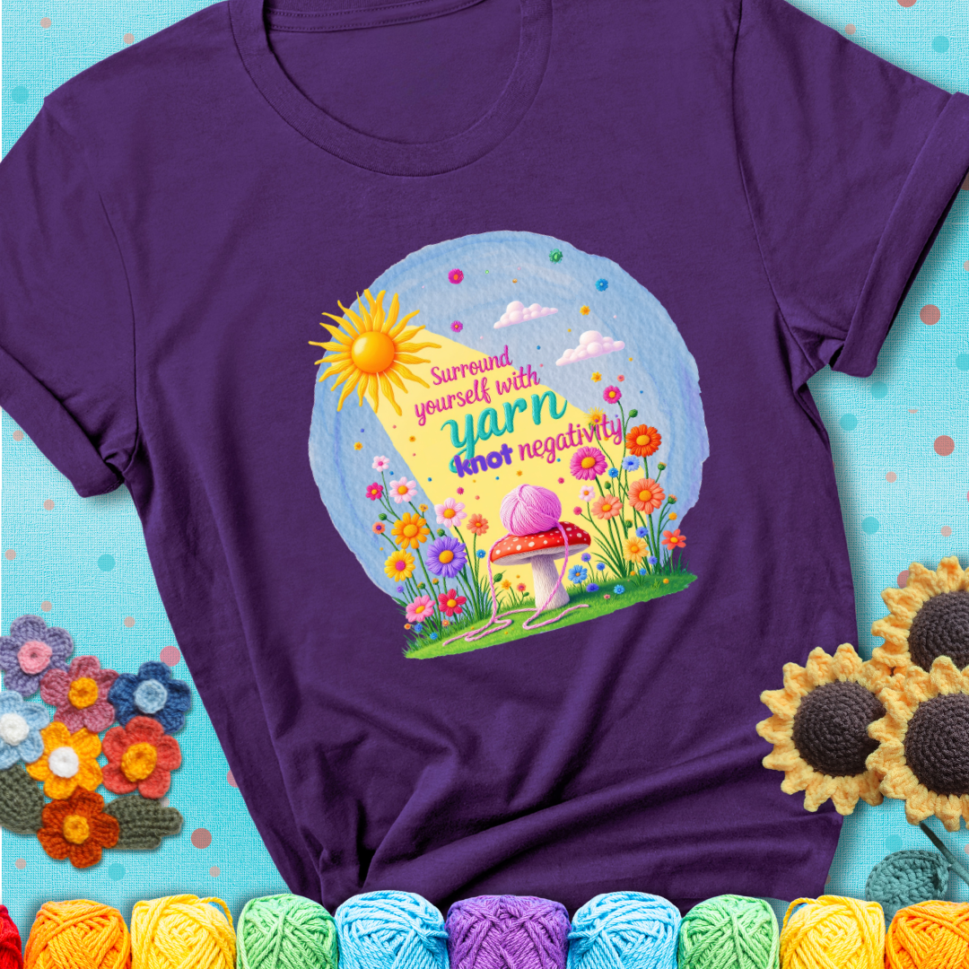 Purple t-shirt featuring a happy spring garden scene with a sunbeam, flowers, and a pink yarn ball on a mushroom, with the quote "Surround yourself with yarn, knot negativity."