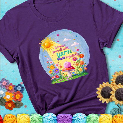 Purple t-shirt featuring a happy spring garden scene with a sunbeam, flowers, and a pink yarn ball on a mushroom, with the quote "Surround yourself with yarn, knot negativity."