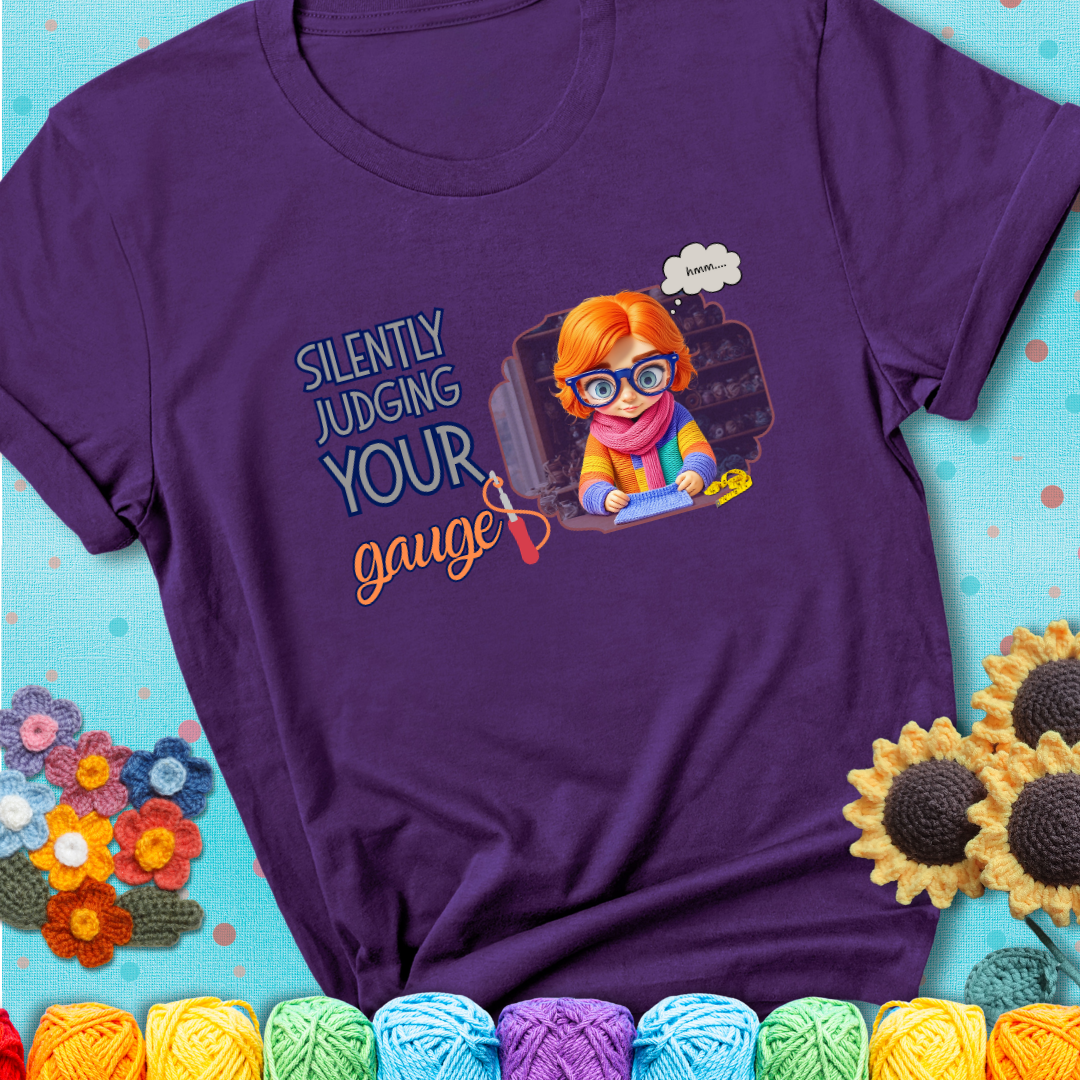 Purple t-shirt with a serious-looking crocheter in rainbow clothing and big glasses, holding a tape measure under the phrase “Silently Judging Your Gauge.”