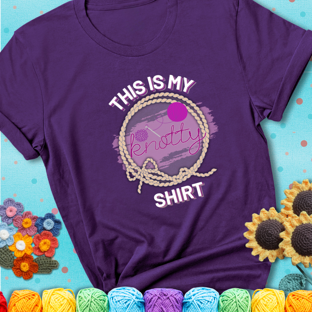 Purple t-shirt with the phrase “This is My Knotty Shirt” inside a rope circle, featuring a yarn ball and crochet hook forming the word “knotty.”