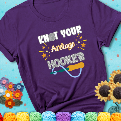 Bold lettering on a purple t-shirt with a yarn hook graphic. Text reads: “I'm Not Your Average Hooker.” A cheeky crochet tee for confident crafters who own their skills.