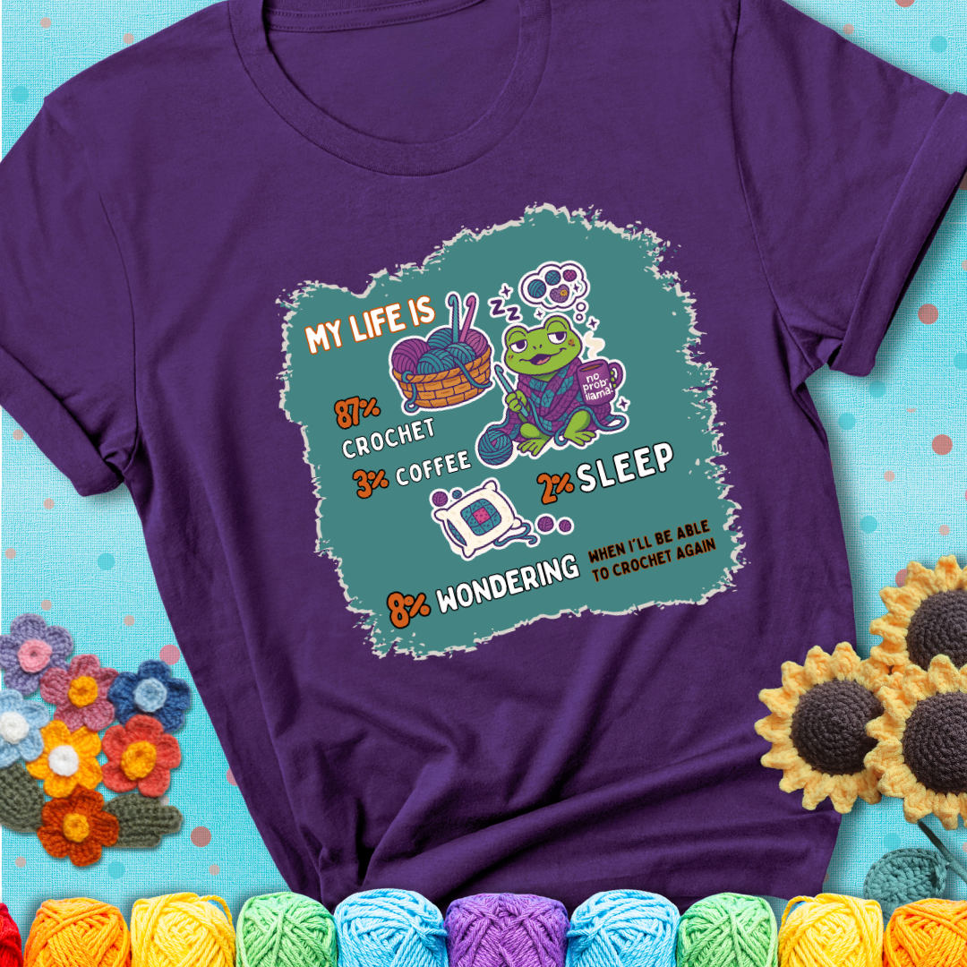 Purple t-shirt with a crocheting frog, coffee, yarn, and text showing a playful life breakdown: 87% crochet, 3% coffee, 2% sleep, 8% wondering when to crochet again.