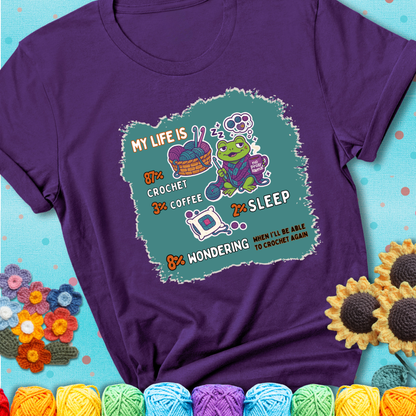 Purple t-shirt with a crocheting frog, coffee, yarn, and text showing a playful life breakdown: 87% crochet, 3% coffee, 2% sleep, 8% wondering when to crochet again.