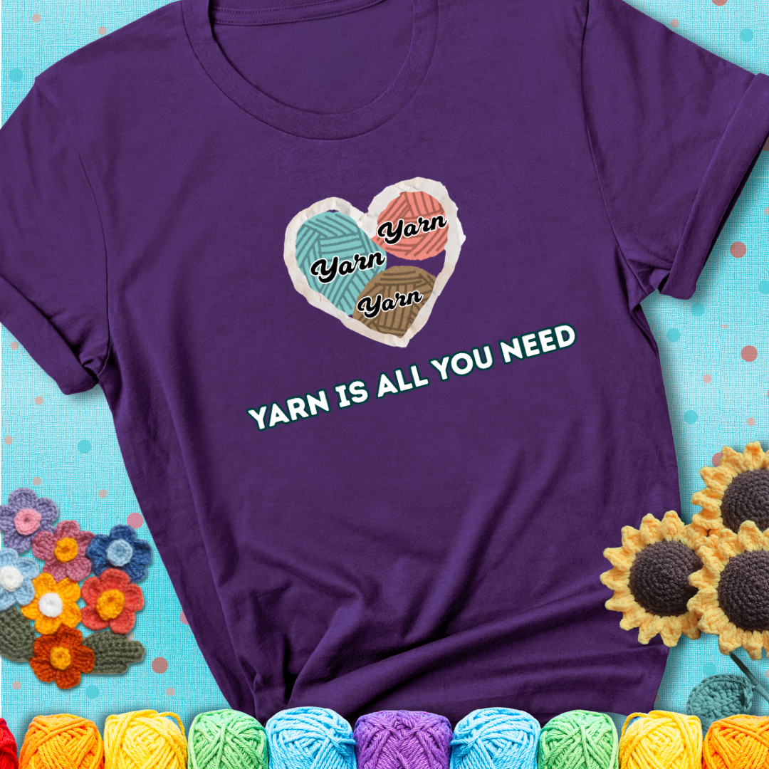 Purple t-shirt with a colorful heart made of yarn textures and the phrase “Yarn Is All You Need” in retro lettering.