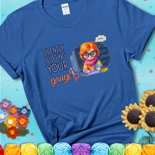 Royal Blue t-shirt with a serious-looking crocheter in rainbow clothing and big glasses, holding a tape measure under the phrase “Silently Judging Your Gauge.”
