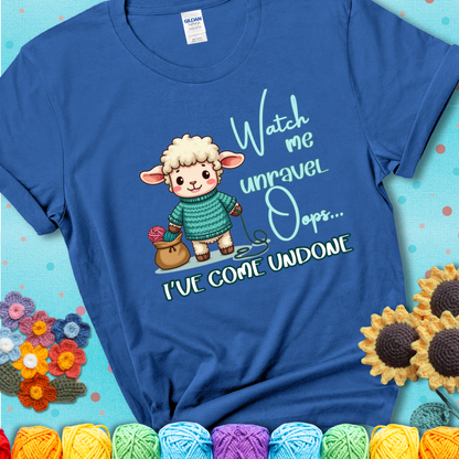 Blue t-shirt with a cute sheep holding yarn looks startled with the phrase “Watch me unravel… Oops, I’ve come undone.” Perfect mix of whimsy and yarn life chaos.