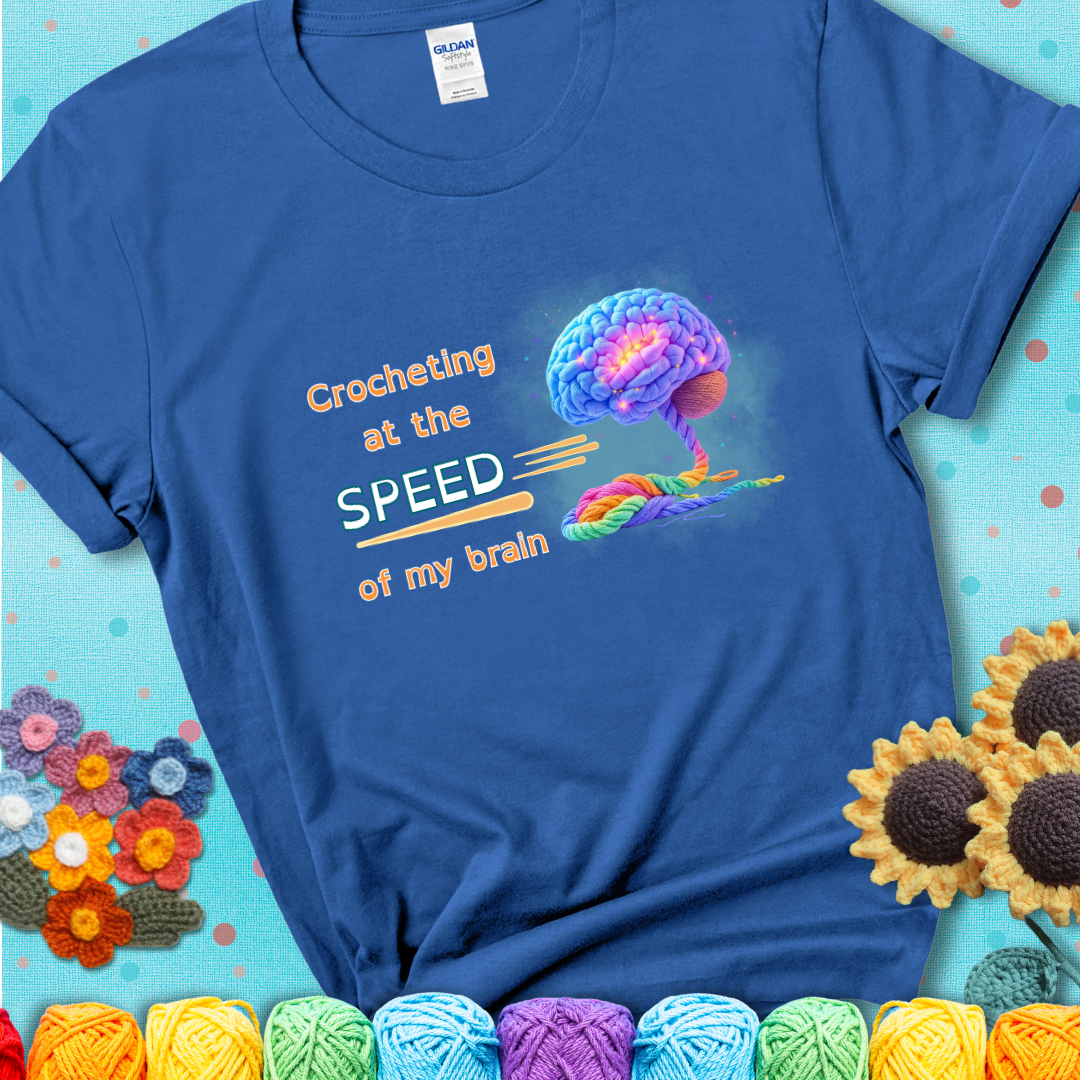 A glowing rainbow brain unravels into colorful yarn with the phrase “Crocheting at the speed of my brain” on a blue t-shirt. 