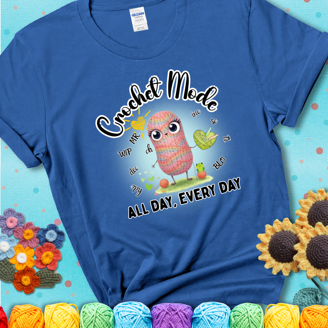 Blue t-shirt with a kawaii-style rainbow yarn character surrounded by crochet stitch abbreviations and holding a yarn heart, with text “Crochet Mode All Day, Every Day.”