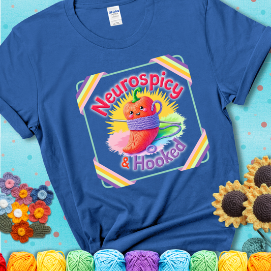 Blue t-shirt featuring a smiling red chili pepper wrapped in yarn with a crochet hook, text says “Neurospicy & Hooked.”