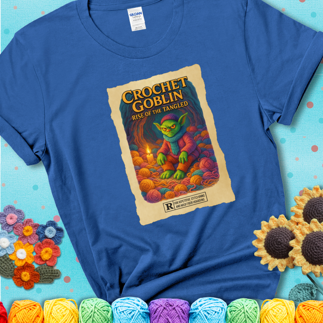 Crochet goblin surrounded by chaotic yarn stash in a cave-like lair. Text reads: “Crochet Goblin: Rise of the Tangled.” A funny fantasy-style blue tee for yarn hoarders and goblin-mode crafters.