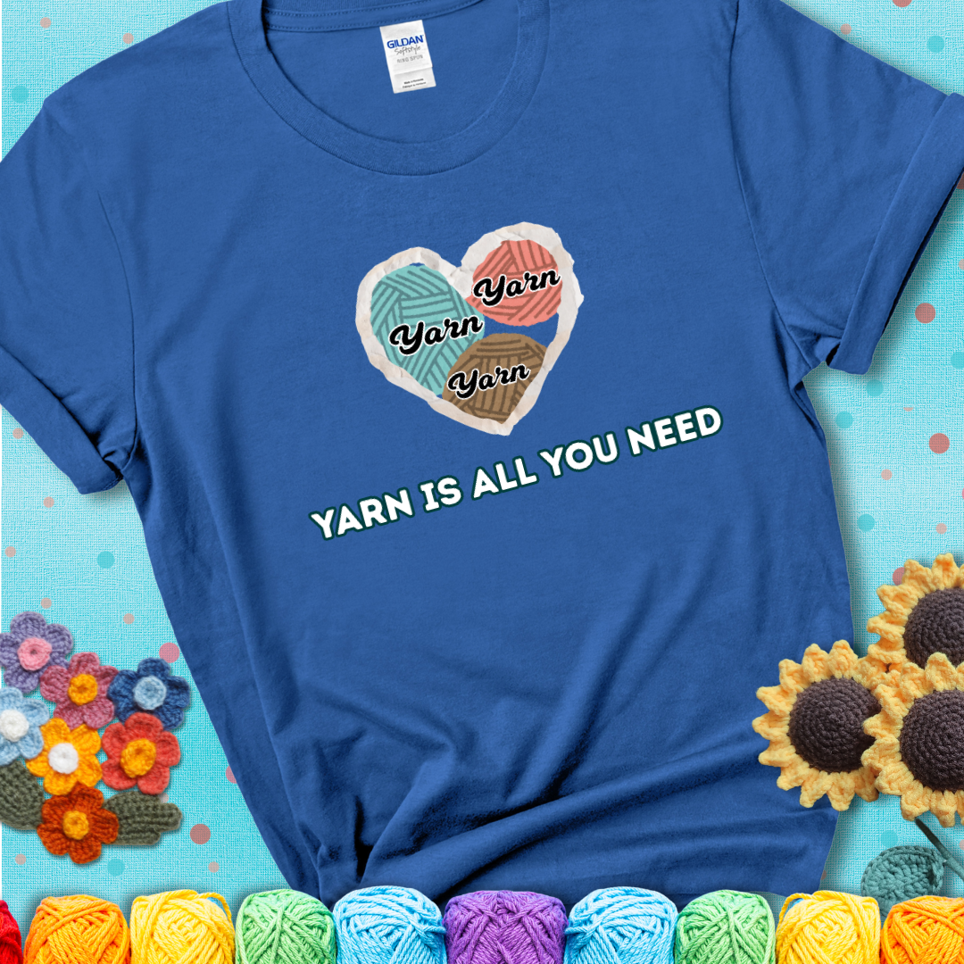 Royal blue t-shirt with a colorful heart made of yarn textures and the phrase “Yarn Is All You Need” in retro lettering.
