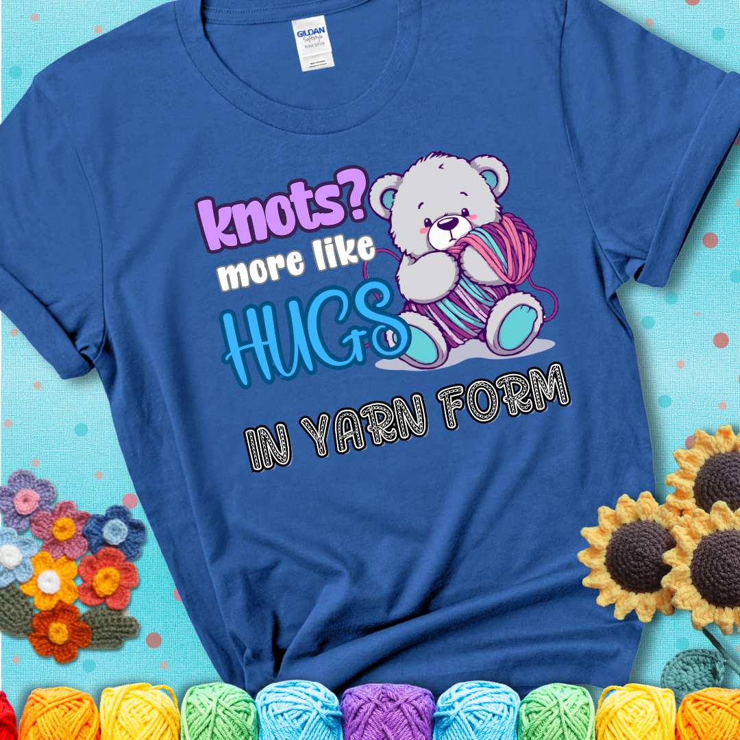 Cute teddy bear holding colorful yarn ball with hearts. Text reads: “Knots? More Like Hugs in Yarn Form.” Perfect for cozy gift-givers and yarn lovers, showing a blue tee with a teal sunflower background